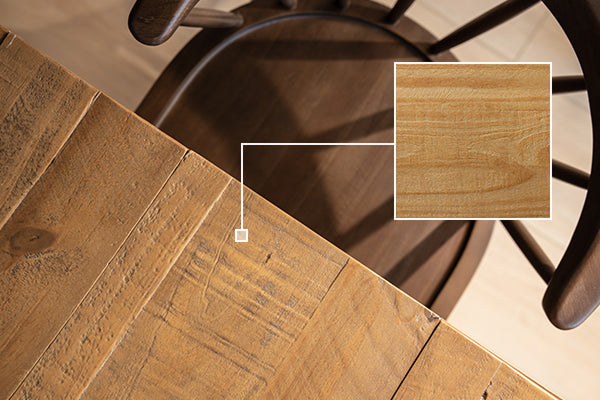 Top-down close-up of a rustic reclaimed wood dining table surface showing detailed wood grain texture with a magnified inset sample and the shadowed seat of a wooden chair