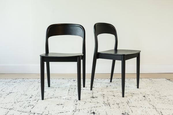 Pair of black modern wooden dining chairs on a textured white patterned rug against a white wall