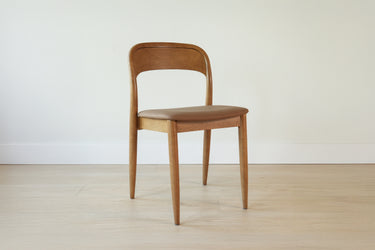 Mid-century modern oak dining chair with curved back and tan leather seat on light hardwood floor, minimalist Scandinavian style