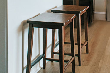 Three counter-height mid-century modern solid wood bar stools with walnut finish lined up against a white kitchen island on hardwood floor