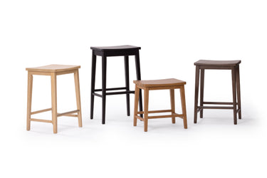 Set of four wooden stools in varying heights and finishes (light wood, medium oak, walnut, dark brown) with square seats and minimalist modern design on white background