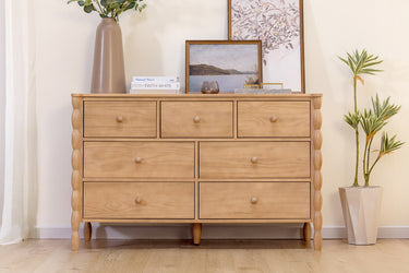 Light wood modern dresser with multiple drawers in bright living room, styled with vase, framed art, books and potted plant