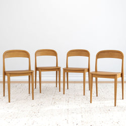 Four elegant wooden dining chairs on a minimalist rug in a modern interior space.