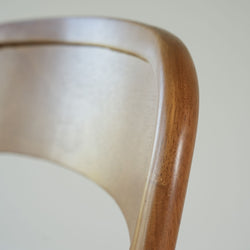Close-up of mid-century modern wooden dining chair back showing warm brown wood grain, curved bent plywood detail and smooth finish
