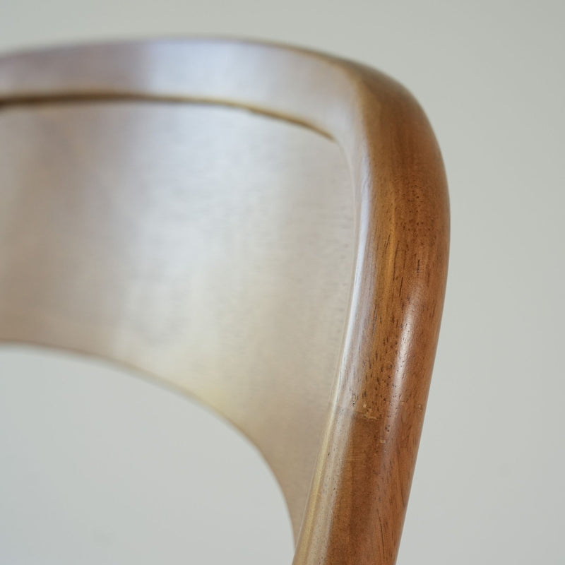 Close-up of mid-century modern wooden dining chair back showing warm brown wood grain, curved bent plywood detail and smooth finish