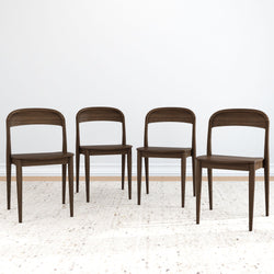 Four elegant, dark wood dining chairs on a light textured rug in a minimalist room setting.