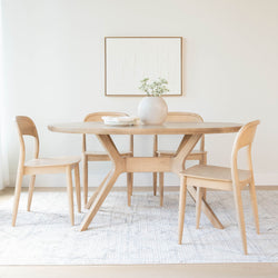 Minimal Scandinavian dining room with round light-wood table and four matching chairs, ceramic vase with white flowers, abstract wall art and neutral area rug