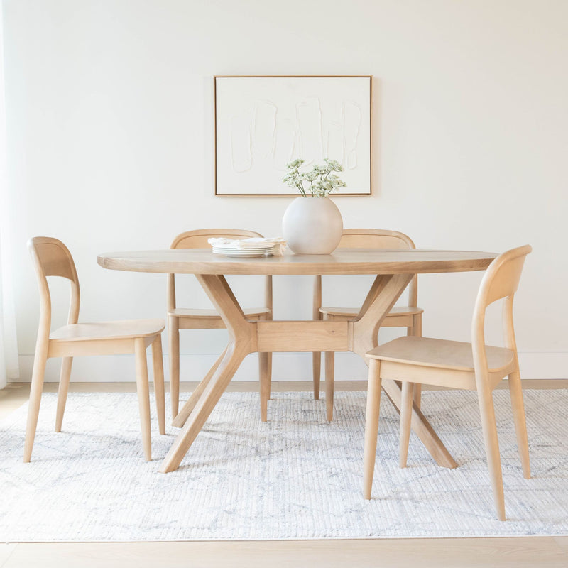 Minimal Scandinavian dining room with round light-wood table and four matching chairs, ceramic vase with white flowers, abstract wall art and neutral area rug