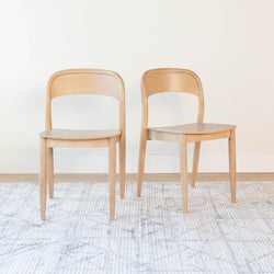 Pair of light wood dining chairs with curved backs in Scandinavian mid-century modern style on a neutral rug