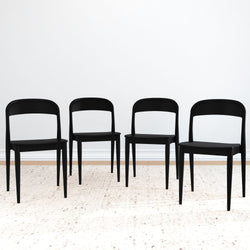 Set of 4 black modern dining chairs on a light area rug in a minimalist dining room with white wall