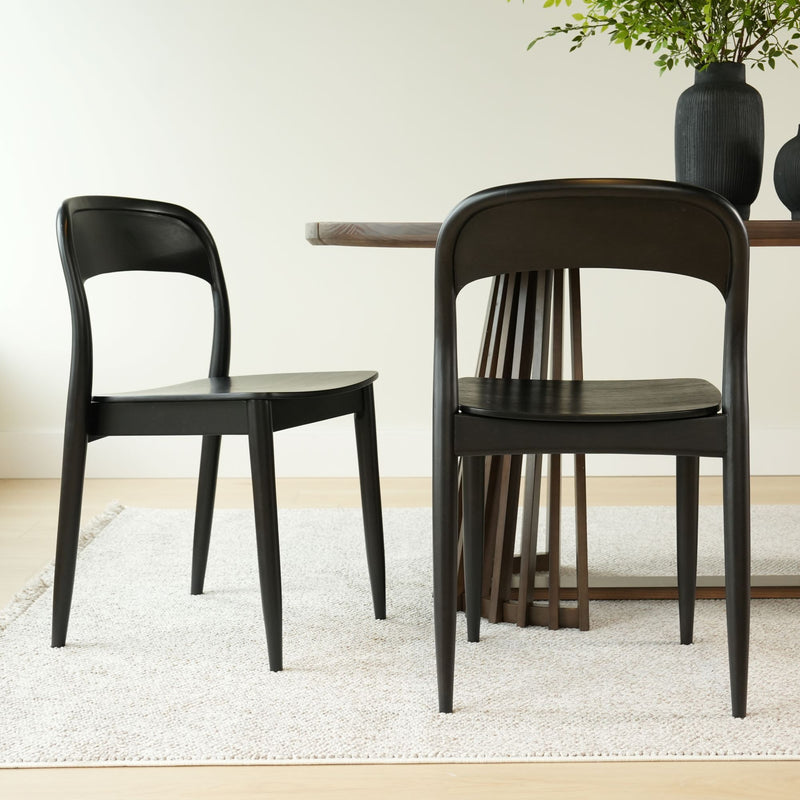 Black wooden dining chairs next to a modern wood dining table on a light neutral rug in a minimalist dining room