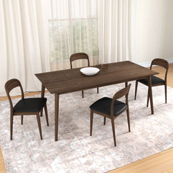 Rectangular mid-century modern walnut dining table set with four black faux-leather chairs, white decorative bowl and glassware on a neutral patterned rug in a bright dining room