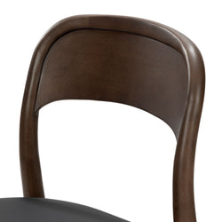 Close-up of mid-century modern walnut wood dining chair with curved backrest and black leather seat