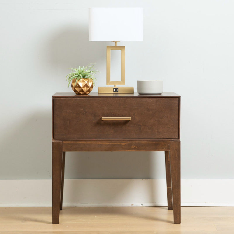Mid-century modern wooden nightstand with drawer, topped with a gold table lamp, small plant in geometric pot, and a ceramic mug, adding style to bedroom decor.