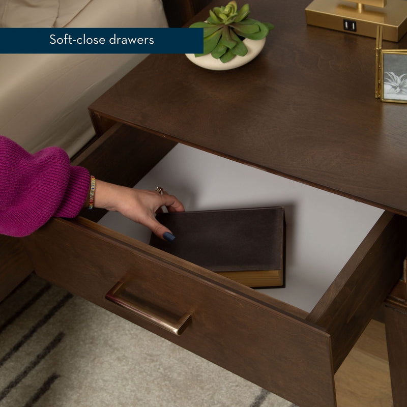 A person placing a book inside a wooden nightstand with soft-close drawers.