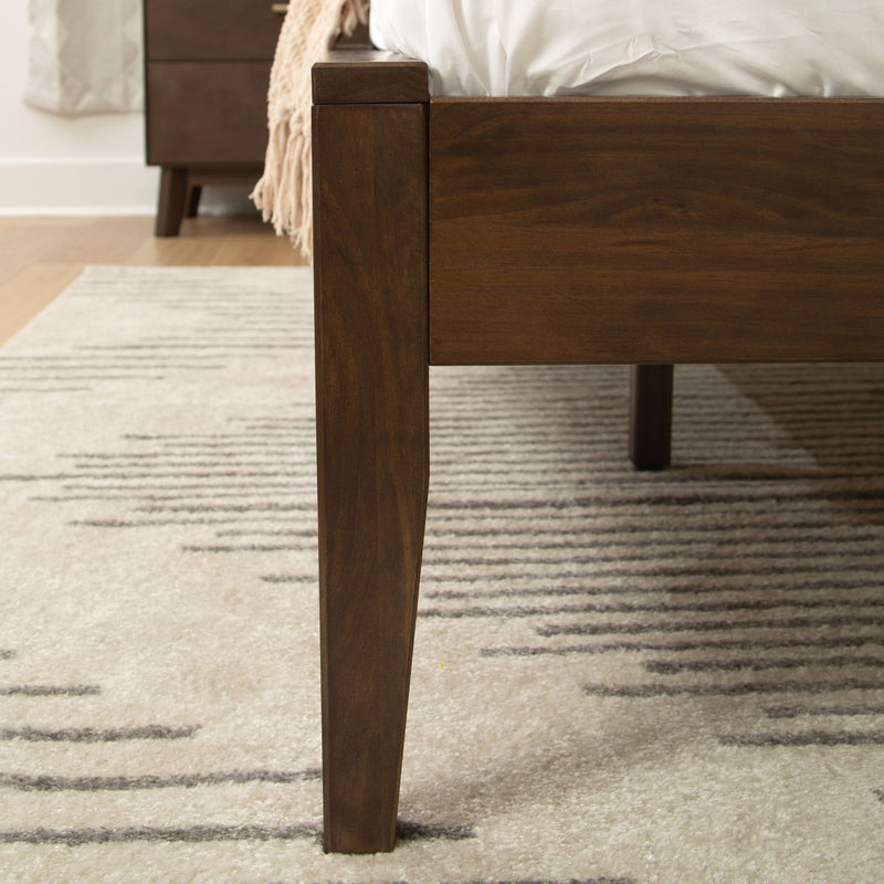 Dark wood bed frame corner with modern design on textured gray and white area rug.