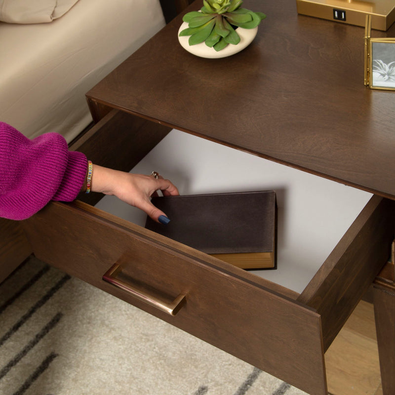 Person placing a book in wooden nightstand drawer next to succulent plant for bedroom organization.