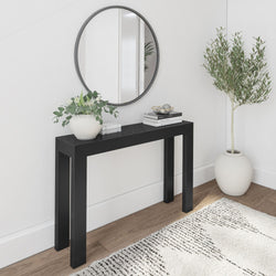Modern minimal entryway with round wall mirror, black console table, white vase of green foliage, stacked books and decorative bowl on wood floor with neutral rug