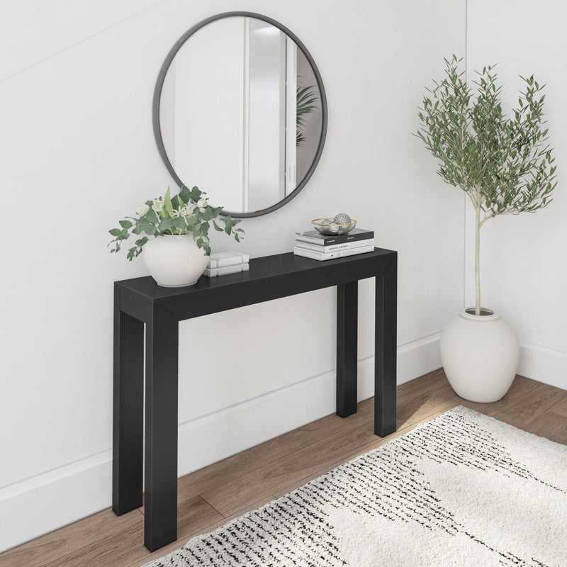 Modern minimal entryway with round wall mirror, black console table, white vase of green foliage, stacked books and decorative bowl on wood floor with neutral rug