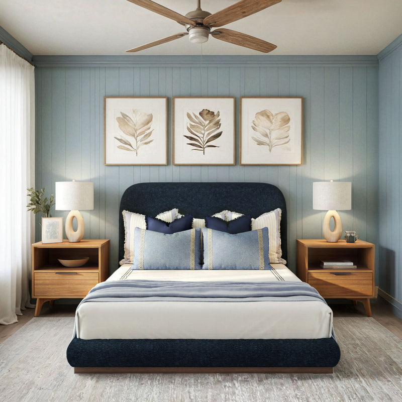 Elegant modern bedroom with navy upholstered bed, stylish lamps, wooden nightstands, and botanical artwork on blue paneled walls.