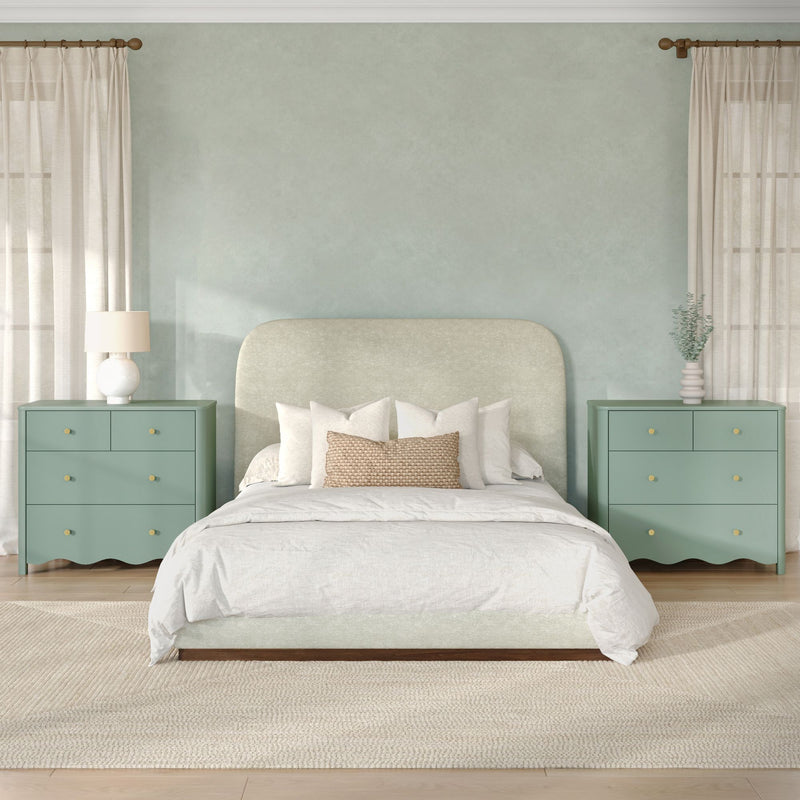 Modern calming bedroom with sage upholstered headboard, matching mint-green nightstands, white bedding, woven accent pillow, table lamps, sheer curtains and potted eucalyptus.