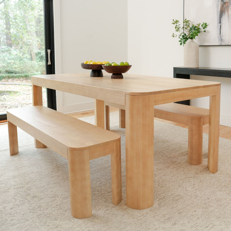 Modern wooden dining table set with benches and fruit bowls in a bright, minimalist dining room.