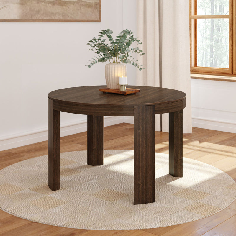 Round wooden dining table with a vase and candle centerpiece in a modern, sunlit room.