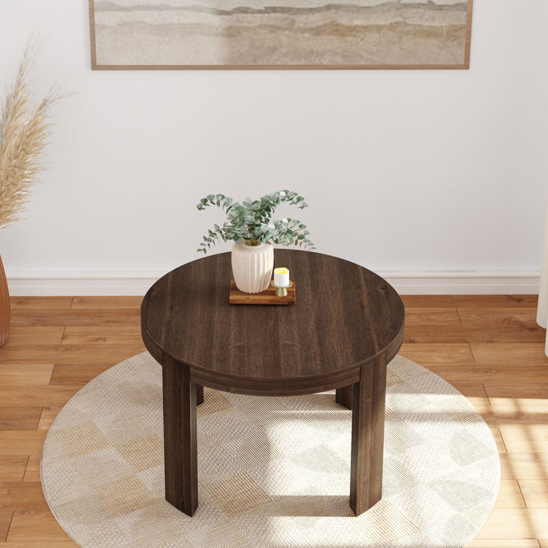 Round wooden coffee table with plant and candle holder in modern living room setting.