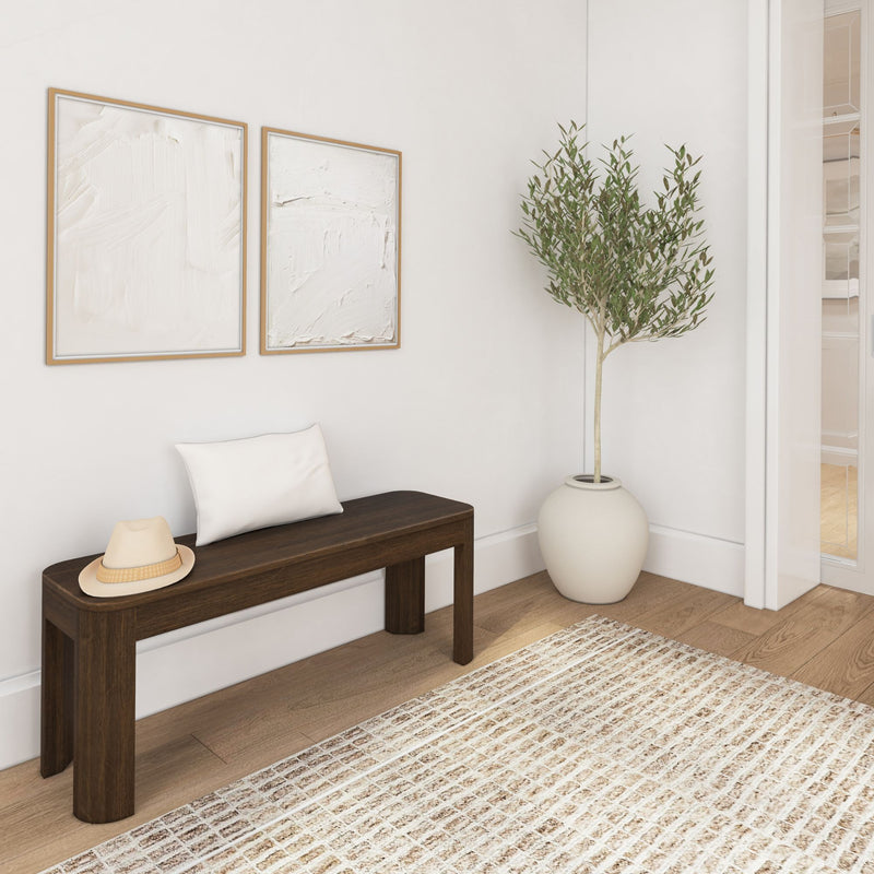 Modern minimalist hallway with wooden bench, decorative hat, cushion, abstract artwork, potted tree, and patterned rug.
