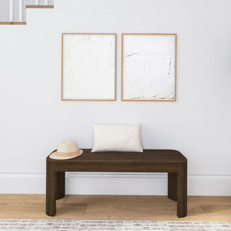 Minimalist hallway decor with wooden bench, hat, pillow, and abstract wall art.