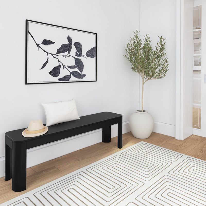 Modern minimalist hallway with black bench, decorative pillow, hat, wall art, potted plant, and geometric rug.