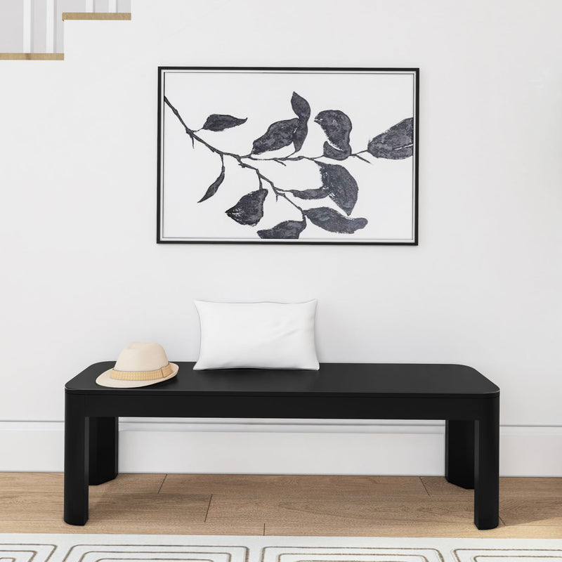 Modern interior design with minimalist black bench, decorative white pillow, beige hat, and abstract leaf artwork on a white wall.