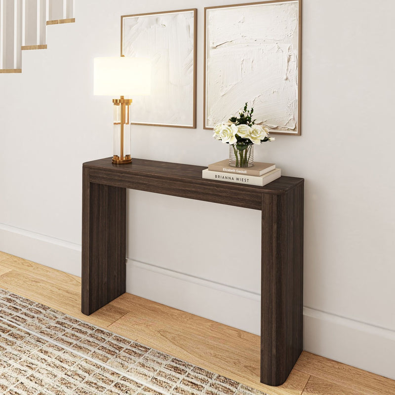 Modern wooden console table with decorative lamp, flowers, and books against a white wall.