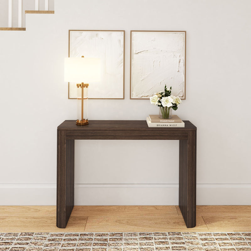 Modern wooden console table with lamp, framed artworks, and decorative flowers in a stylish home interior.