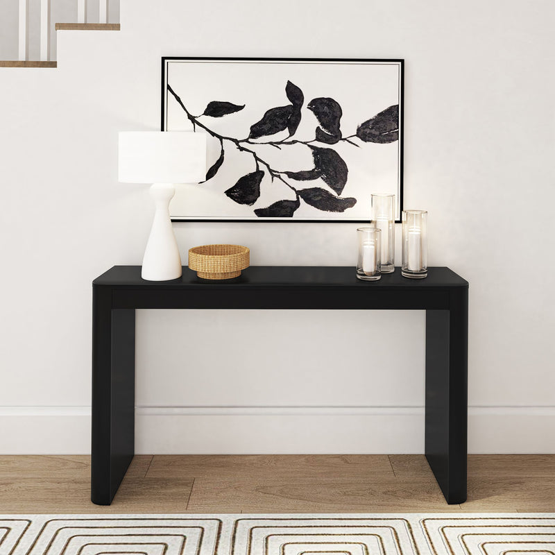 Modern black console table with decorative items, including a lamp and candles, under minimalist artwork in a contemporary home setting.