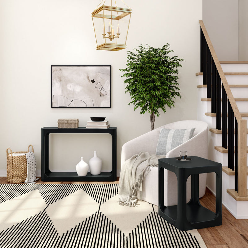 Modern living room interior with black and white decor, featuring a cozy armchair, abstract wall art, geometric rug, and potted plant next to a staircase.