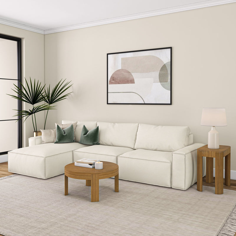 Contemporary living room with modern beige sofa, round wooden coffee table, green pillows, abstract wall art, and indoor plant decor.