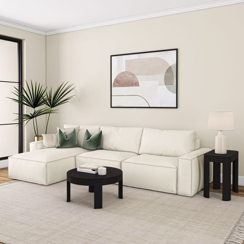 Modern living room with a white sectional sofa, black coffee table, abstract wall art, and decorative pillows.