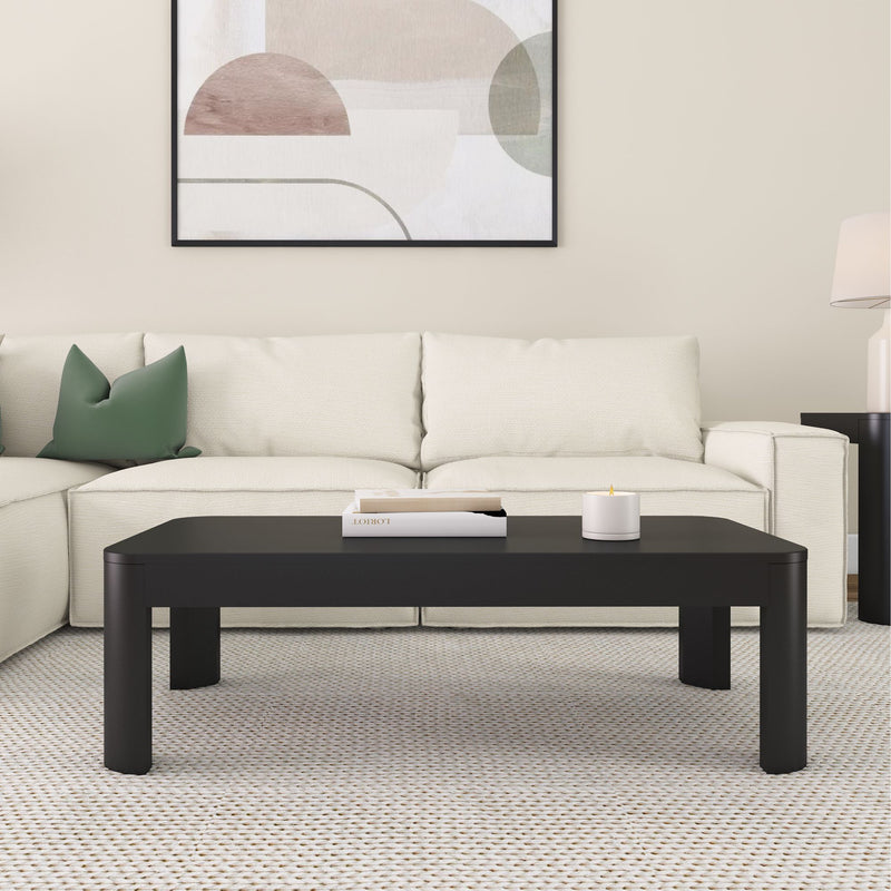 Modern living room with a black coffee table, white sofa, green pillow, and abstract wall art.