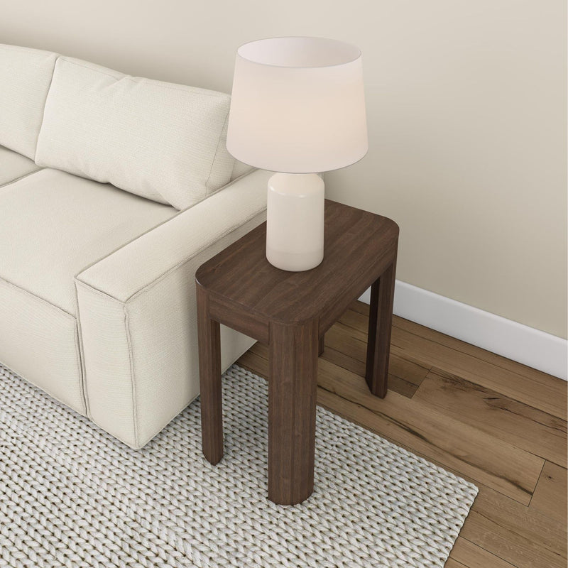 Cozy living room with a stylish wooden side table and modern lamp next to a white sofa on a textured rug.