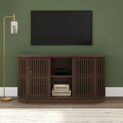 Dark wood slatted media console with bowl and stacked books under wall-mounted TV on green accent wall with gold floor lamp