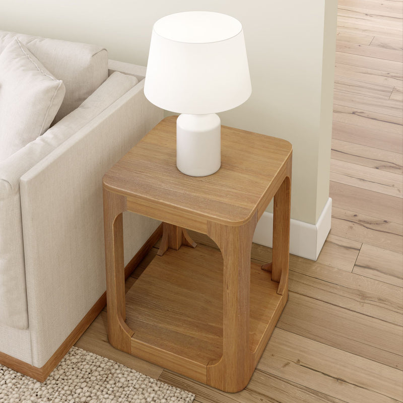 Wooden side table with a white lamp next to a beige sofa on a hardwood floor.