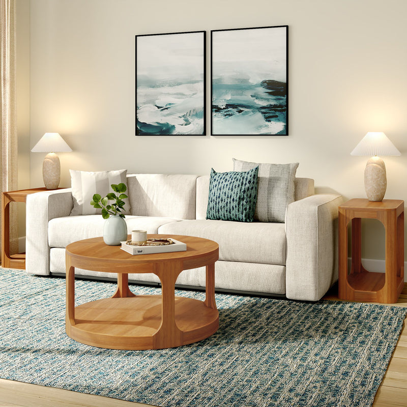 Modern coastal living room with cream sectional sofa, round wooden coffee table, teal patterned rug, abstract ocean wall art, wooden side tables, table lamps, and decorative pillows