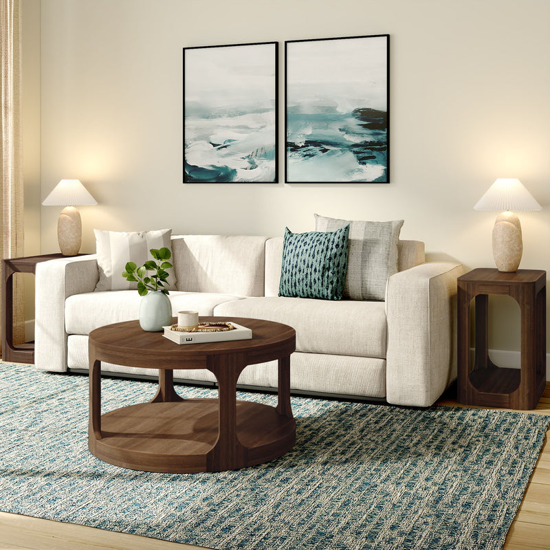 Modern neutral living room with beige sofa, teal accent pillows, round walnut coffee table, blue textured area rug, wooden side tables with lamps and abstract ocean wall art