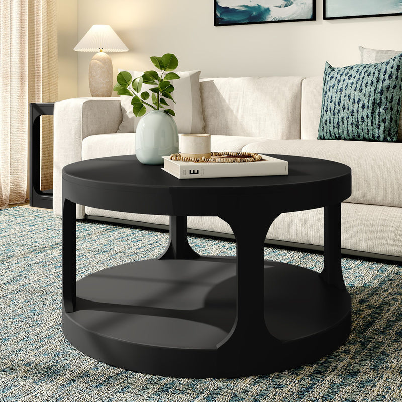 Modern matte black round coffee table styled with a vase, book and tray in a neutral living room featuring a white sofa and blue patterned rug.
