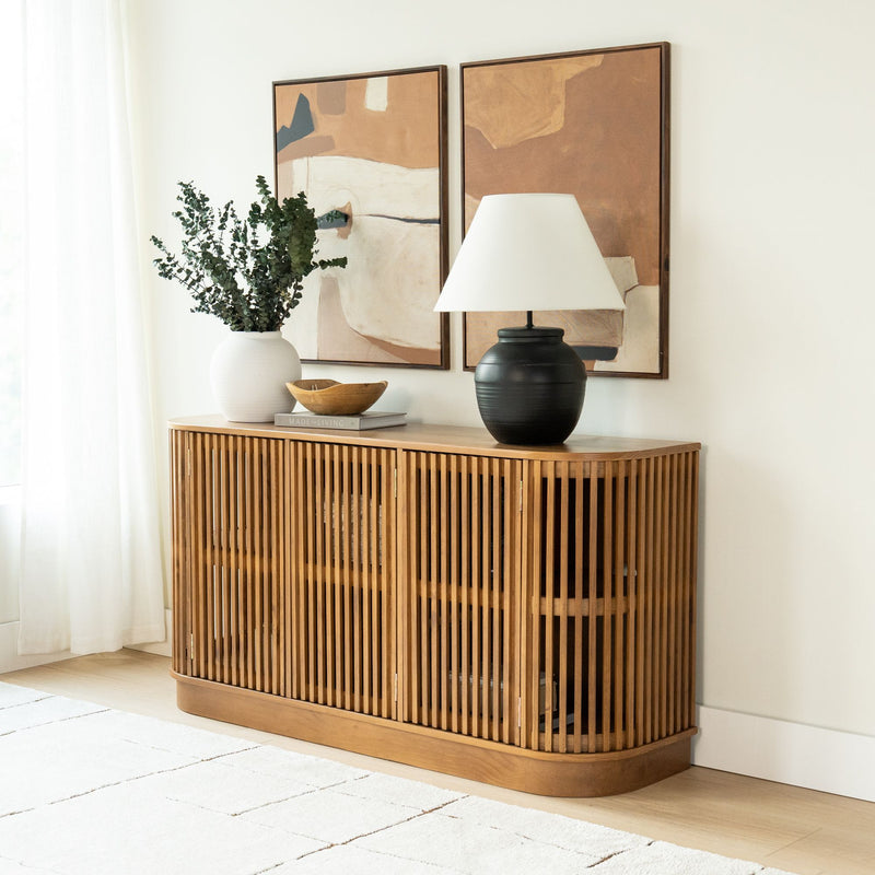 Light-wood slatted console cabinet in modern boho living room with black ceramic lamp, white vase of eucalyptus, and abstract wall art