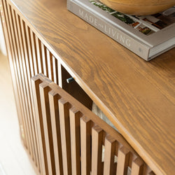 Close-up of mid-century modern slatted oak media console with curved top, decorative wooden bowl and "Made for Living" coffee table book — living room decor.