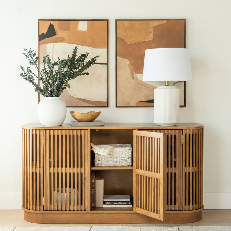 Natural slatted wood entryway console cabinet with eucalyptus in white vase, table lamp and abstract tan wall art
