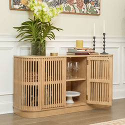 Modern wooden sideboard with open shelving, decorative plants, books, and candles in a stylish living room setting.