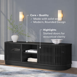 Black modern wooden TV console with slatted doors for acoustical clarity, featuring a rounded design, decorative vase, and bowl.
